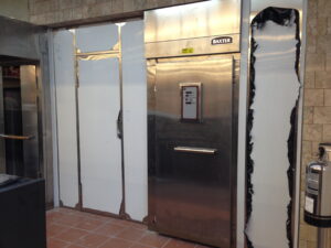 Elevator doors in a tiled lobby with peeling white protective panels and a stainless steel finish; a fire extinguisher visible to the right.