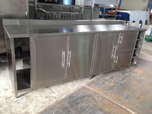 Stainless steel commercial kitchen island with cabinets in a workshop setting.