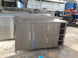 Industrial stainless steel kitchen cabinet with drawers and doors in a workshop setting.