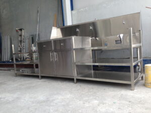 Industrial stainless steel workbench with multiple drawers and a raised backsplash in a workshop setting