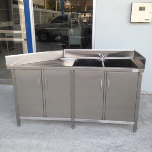 Outdoor stainless steel barbecue grill station with lower cabinets, set on a concrete surface. Reflections of a car appear in the glass behind it.