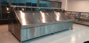 Large stainless steel refrigerated display counter on wheels in a bright, modern room.